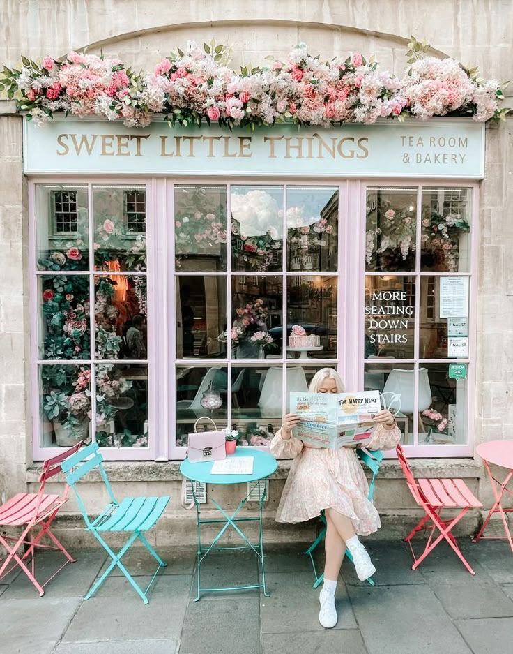 a woman sitting at a table in front of a store with flowers on the window