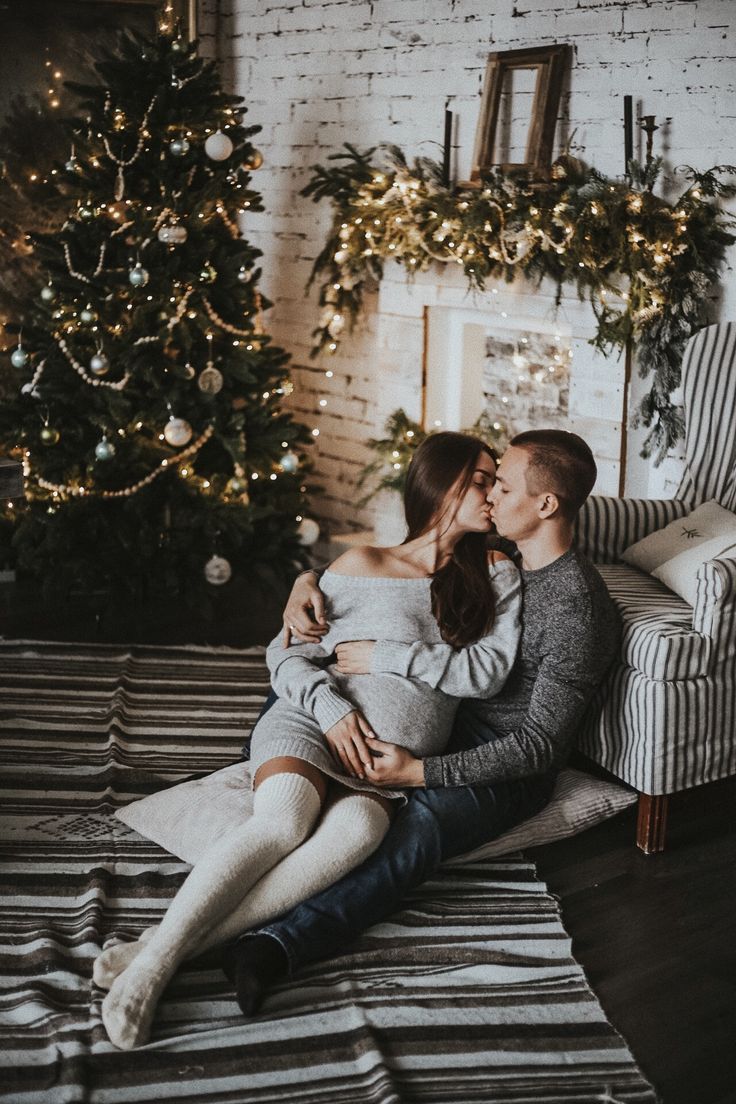 a man and woman sitting on a couch in front of a christmas tree with lights