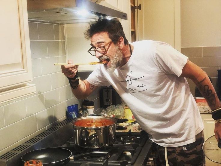 a man standing in front of a stove holding a wooden spoon