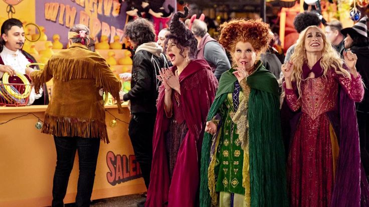 three women dressed in costume standing next to each other at a carnival booth with clowns on the sidelines