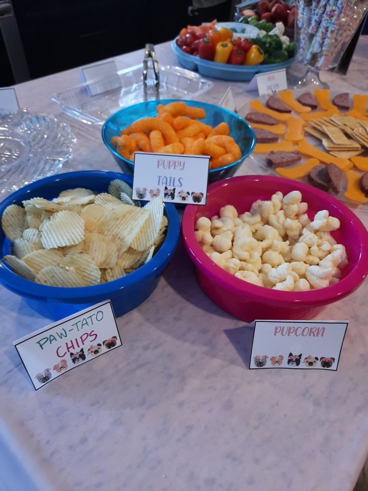 several bowls filled with chips on top of a table next to plates of fruit and vegetables