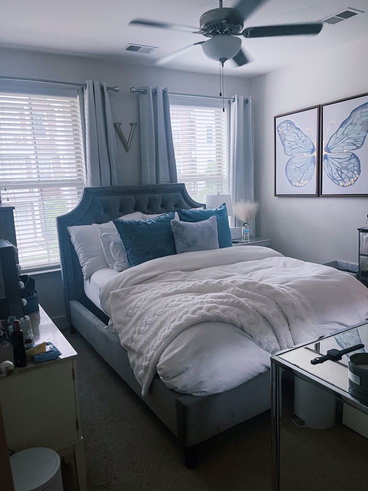 a bedroom with a bed, dresser and ceiling fan in front of two windows that have butterfly paintings on them