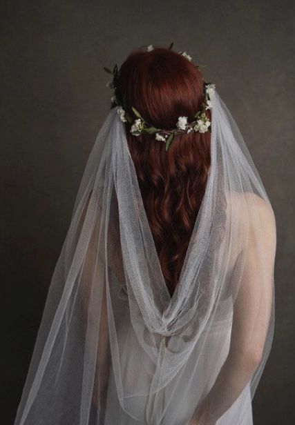 a woman with red hair wearing a veil and flowers in her hair is shown from the back