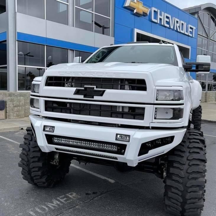 a white truck is parked in front of a chevrolet dealership with large tires on it