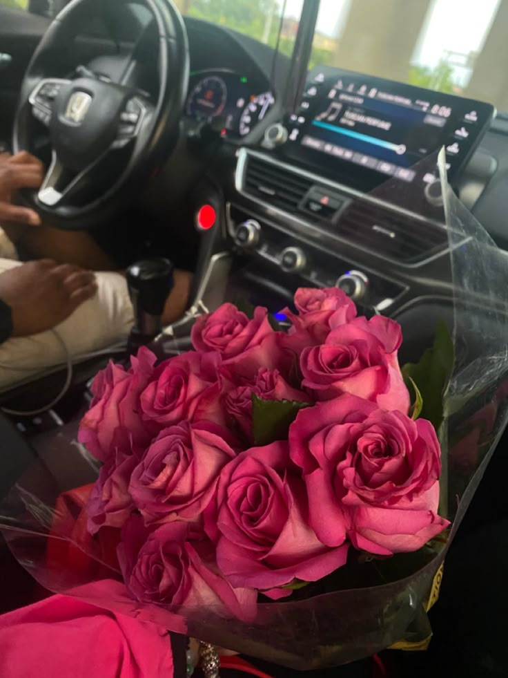 a bunch of pink roses sitting in the center of a car with steering wheel and dashboard