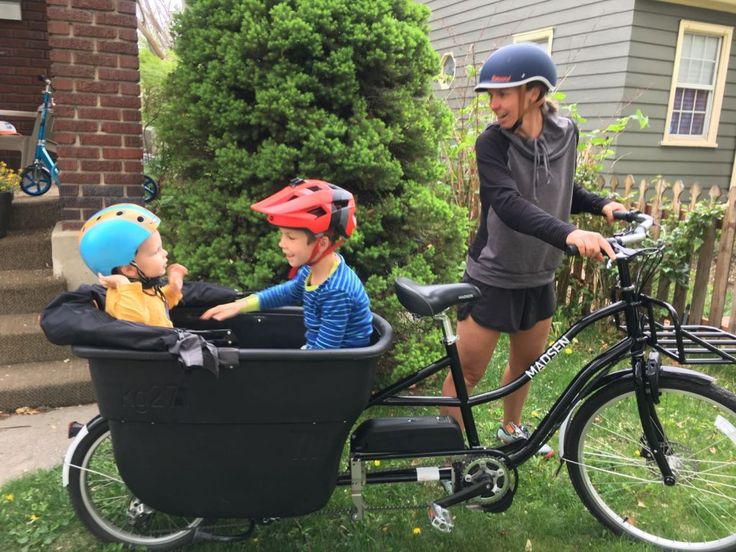 two children in a bike trailer with helmets on and one child sitting in the basket