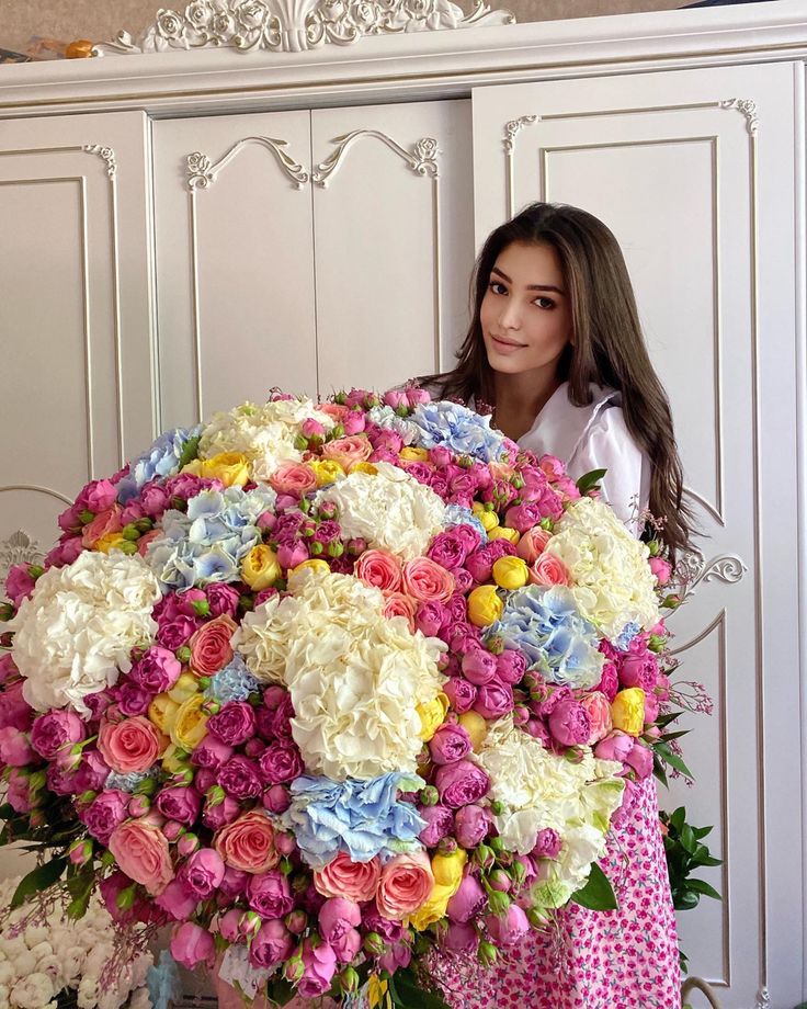 a woman holding a large bouquet of flowers in front of a white cabinet with drawers