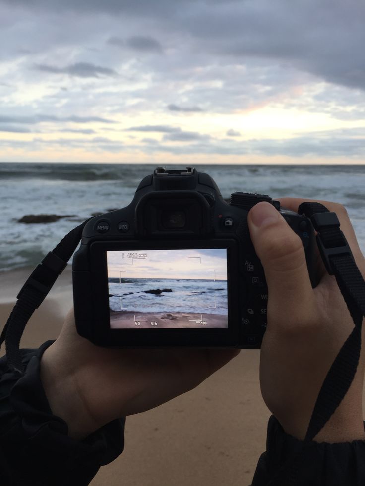 a person holding up a camera to take a photo on the beach with waves in the background