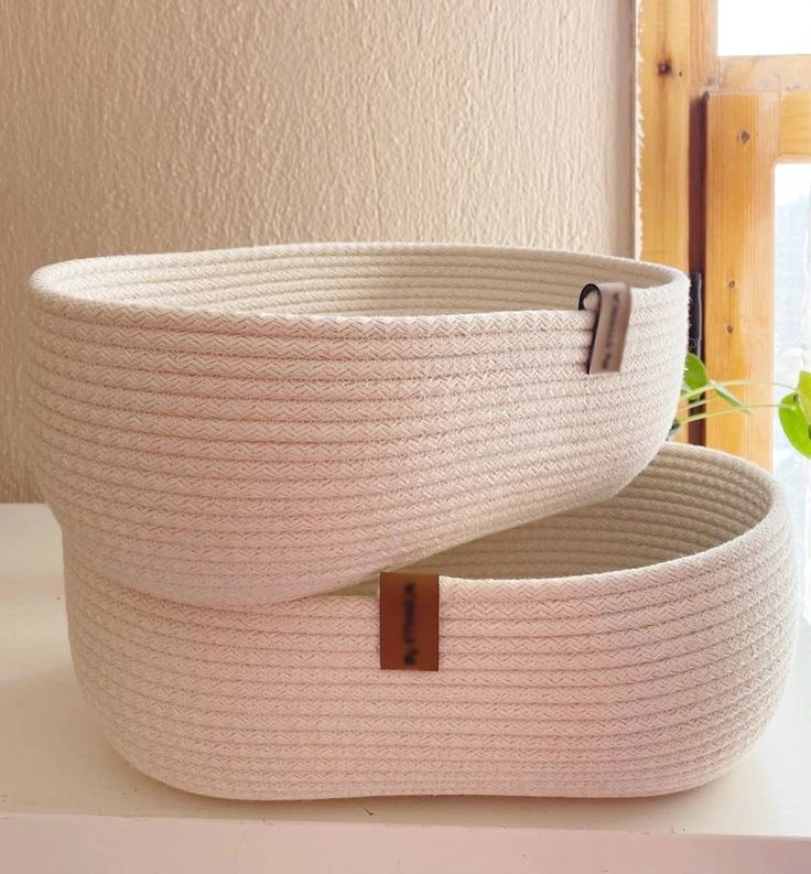 two white baskets sitting on top of a counter next to a window with a plant in it