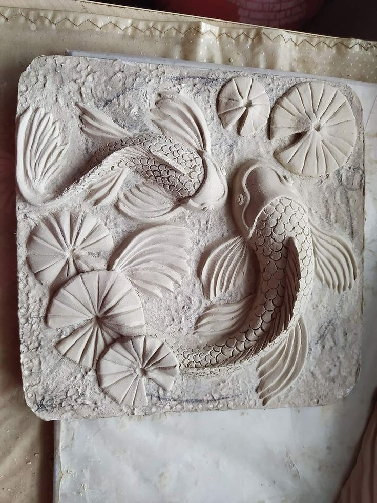 an intricately carved white tile with flowers and fish on the bottom, sitting on top of a marble slab