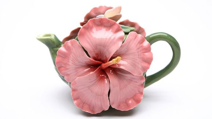 a pink flower sitting on top of a green tea pot