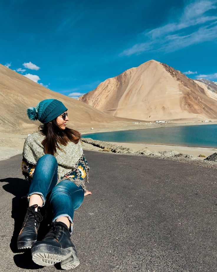 a woman sitting on the side of a road next to a lake