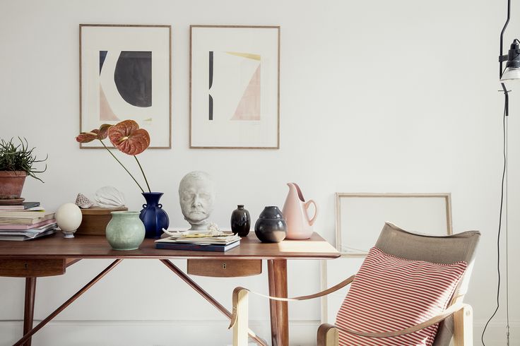 a wooden table topped with vases sitting next to a chair and painting on the wall