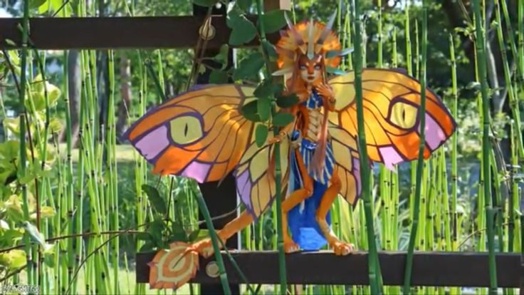 a colorful butterfly statue sitting on top of a lush green field next to tall grass