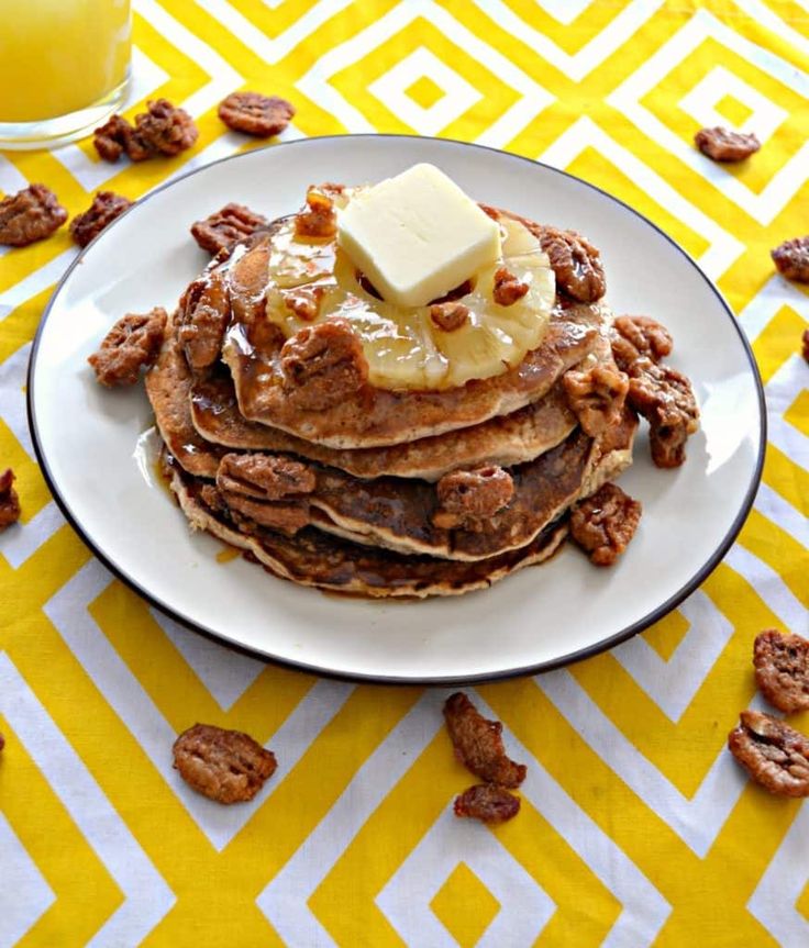 a stack of pancakes topped with butter and walnuts on a plate next to a glass of orange juice