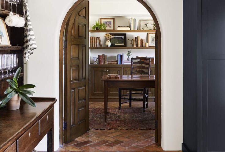 an arched doorway leading to a dining room with a table and bookshelf in the background