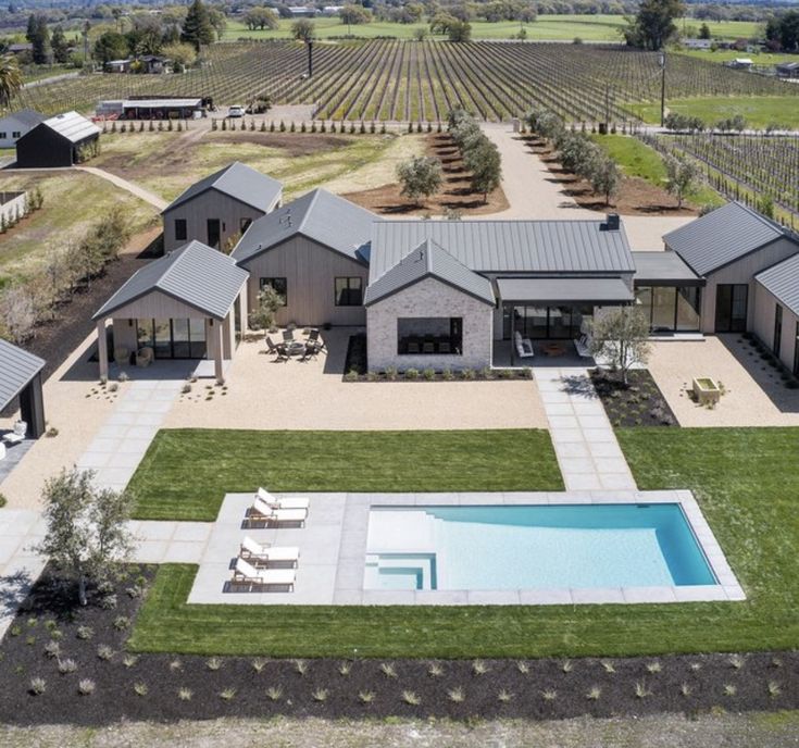 an aerial view of a house with a swimming pool in the foreground and vineyards in the background