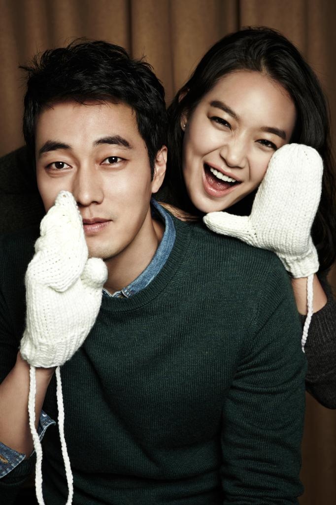 a man and woman sitting next to each other with mittens on their hands, smiling