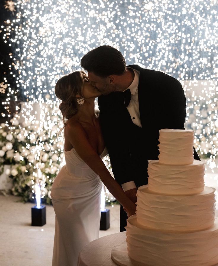 a bride and groom kissing in front of a wedding cake with white lights behind them