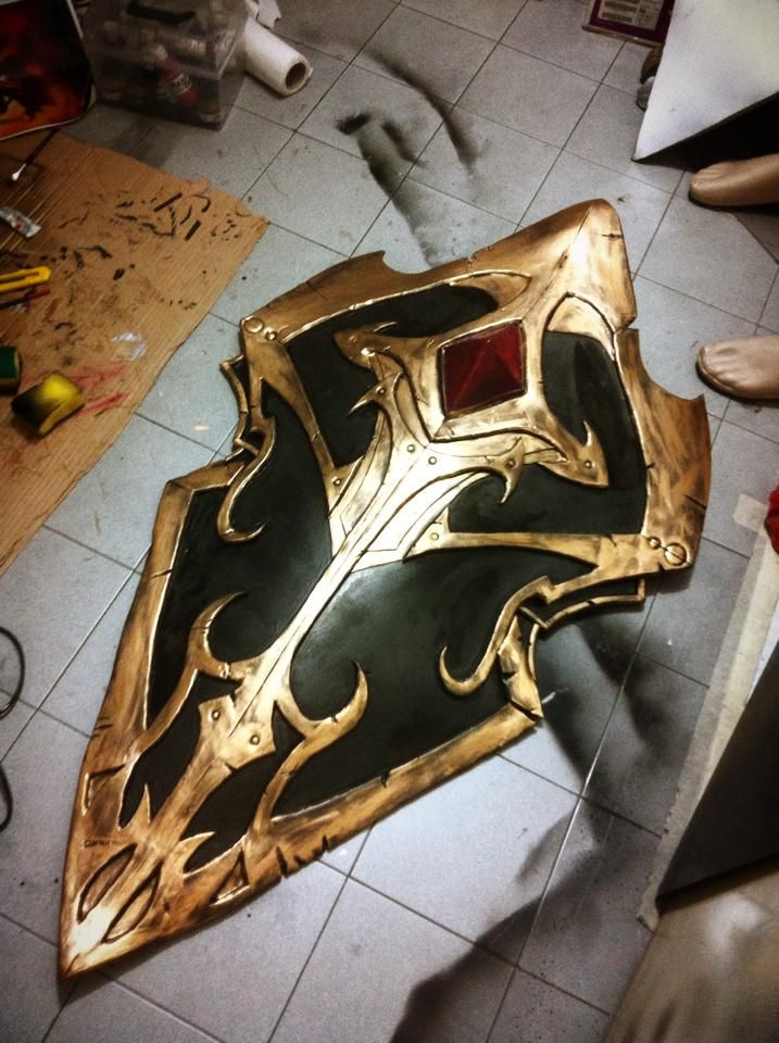 a gold and black shield sitting on top of a tile floor next to a knife