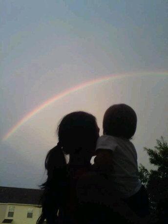 two children are standing in front of a rainbow and the sky is dark with no clouds