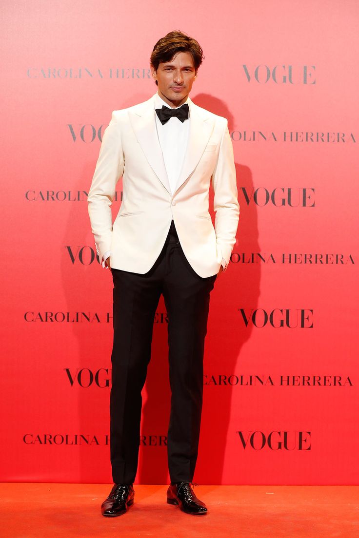 a man in a white tuxedo and black bow tie standing next to a red wall