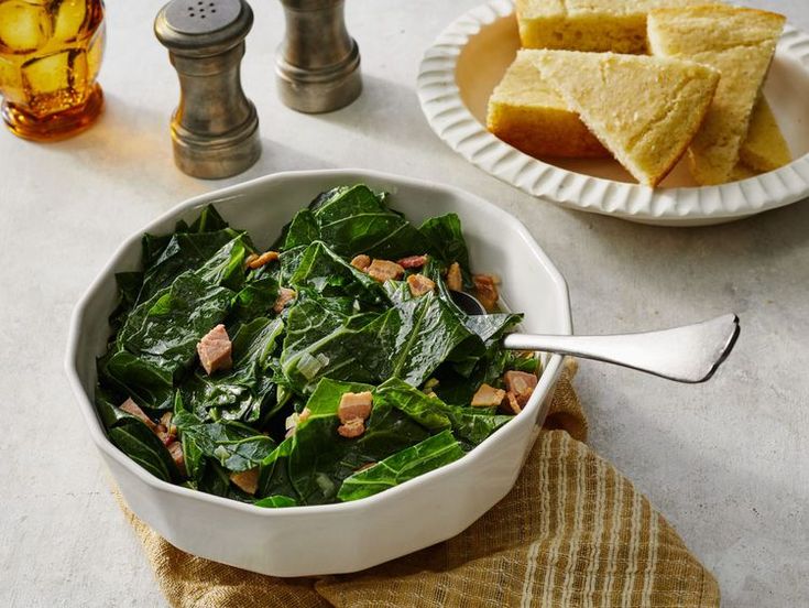 a white bowl filled with spinach next to two plates of cornbreads on a table