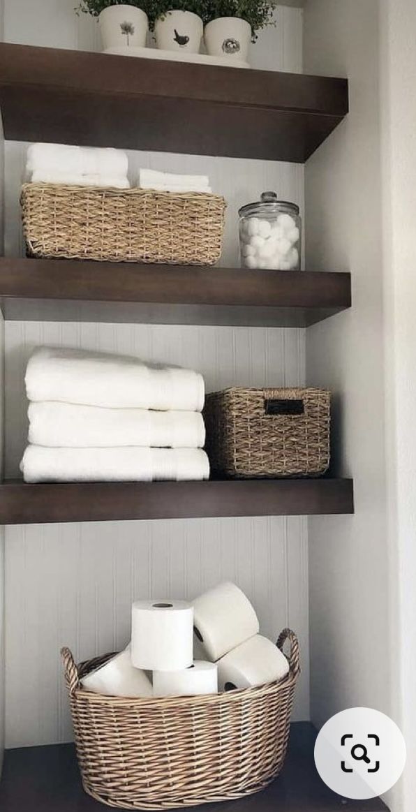 bathroom shelves with towels and baskets on them in the corner, next to toilet paper