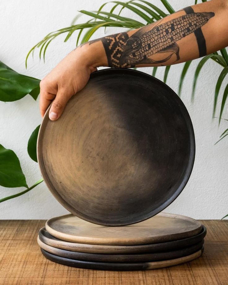 a person holding a black plate on top of a wooden table next to a plant