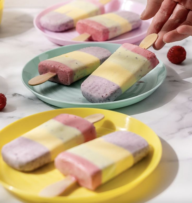 two plates with popsicles on them and strawberries in the background, one being dipped with ice cream