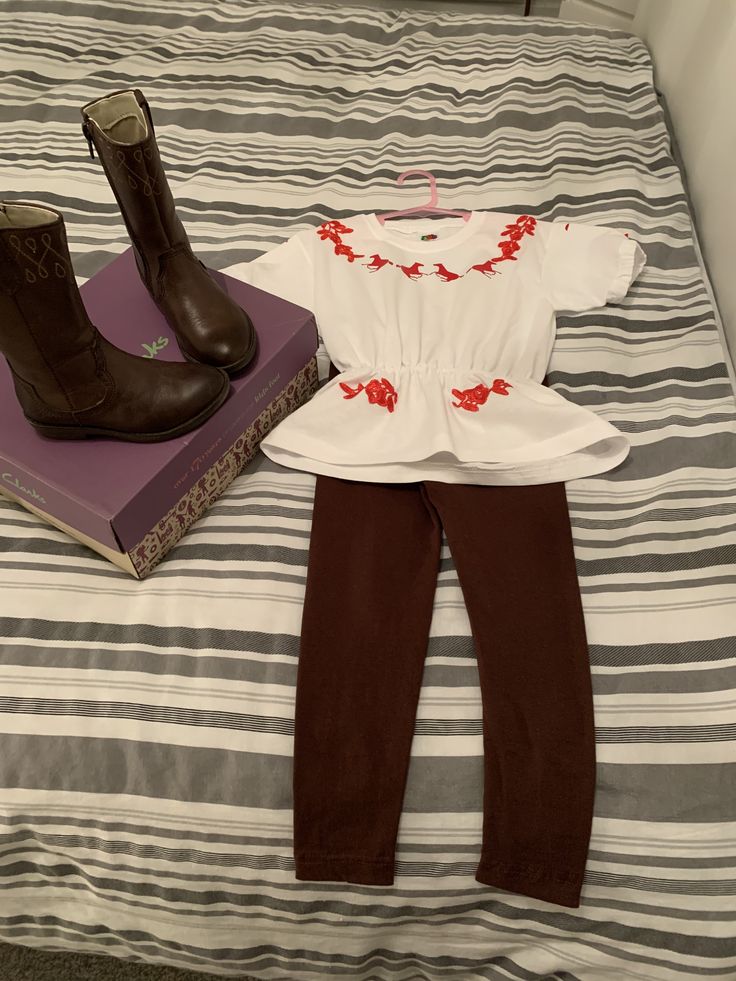 a pair of brown boots sitting on top of a bed next to a white shirt