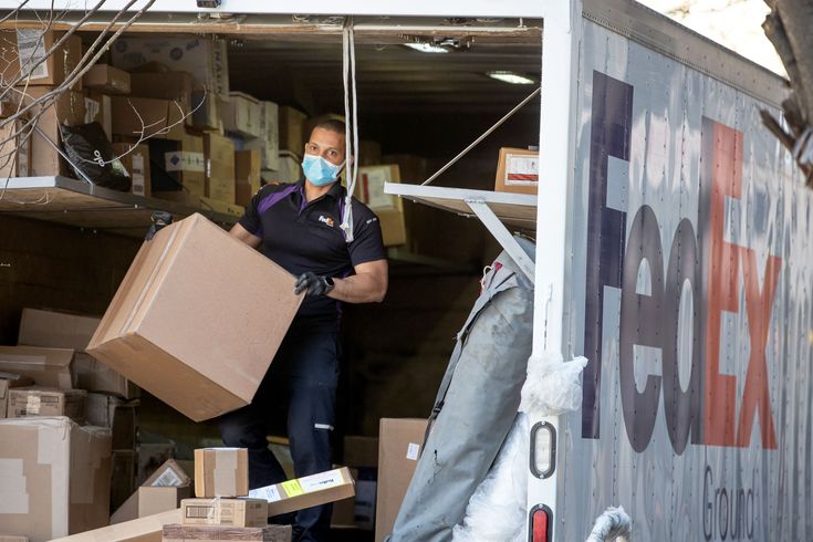 a man wearing a face mask is unloading boxes from the back of a moving truck