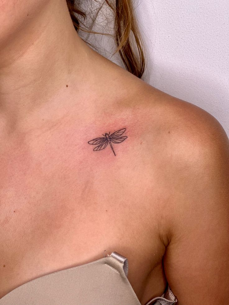 a woman's chest with a small dragonfly tattoo on her left side shoulder