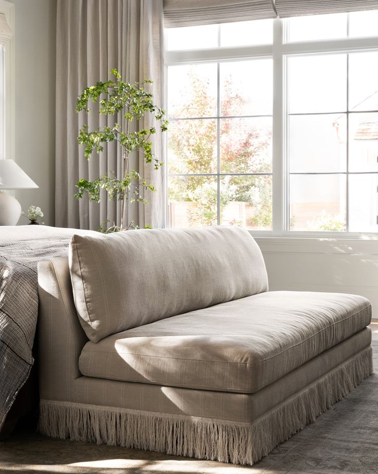 a white couch sitting next to a window in a room with curtains on the windowsill