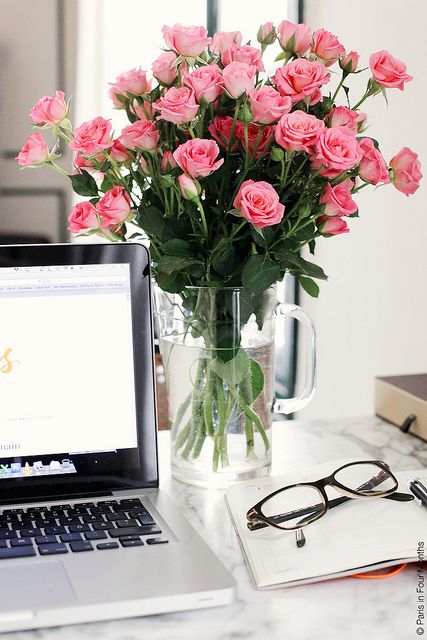 an open laptop computer sitting on top of a desk next to a vase with flowers