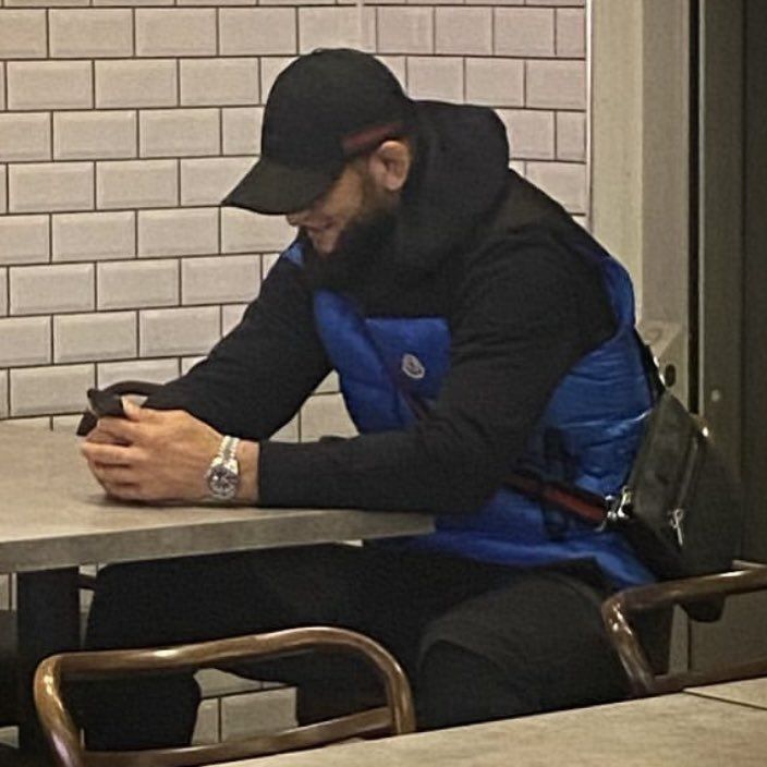 a man sitting at a table looking at his cell phone while wearing a black hat