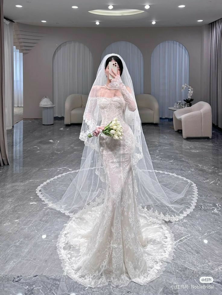 a woman in a white wedding gown and veil standing on a circular floor with her hands to her face