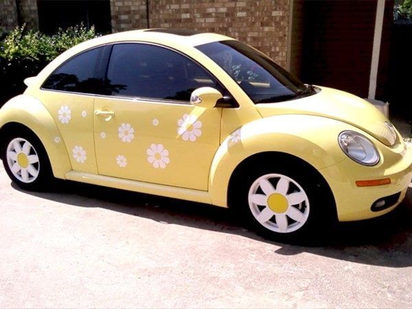 a yellow car with white flowers painted on it's side parked in front of a brick building