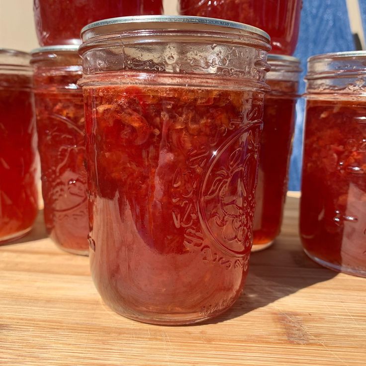 several jars filled with red liquid sitting on top of a wooden table next to each other