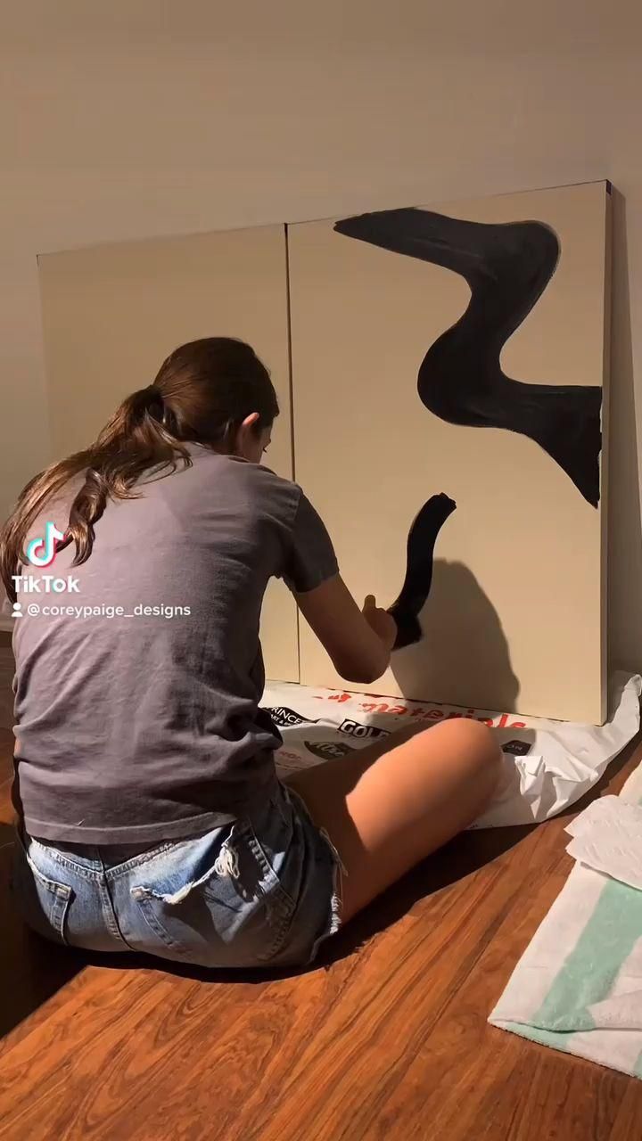 a woman is sitting on the floor painting a wall with an abstract art piece in front of her