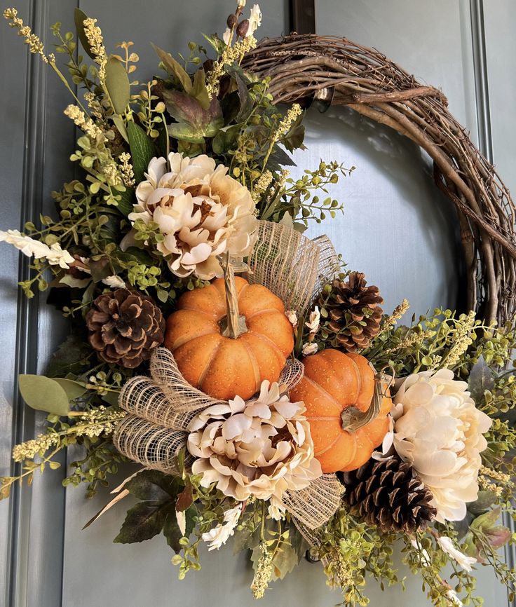 a wreath with pumpkins, flowers and pine cones is hanging on the front door