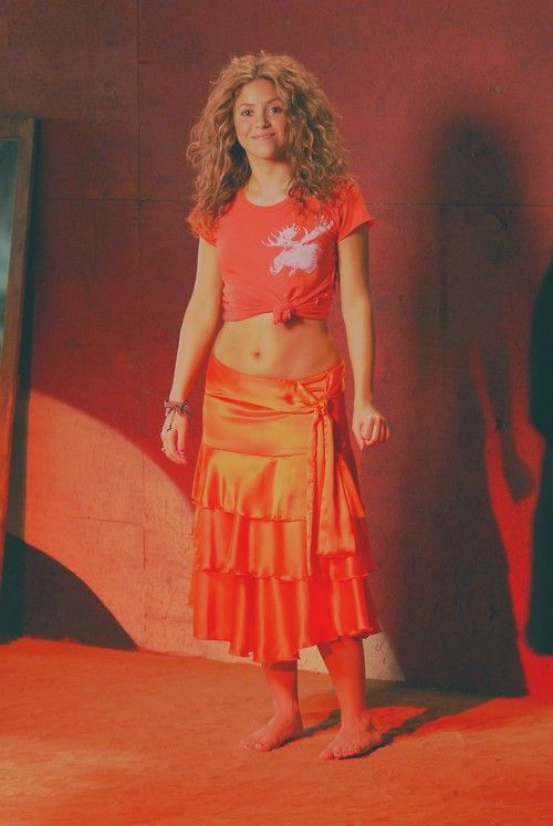 a woman standing in front of a wall wearing an orange skirt and t - shirt