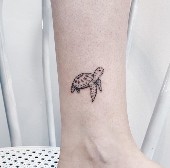 a small turtle tattoo on the ankle by a woman's foot in black ink