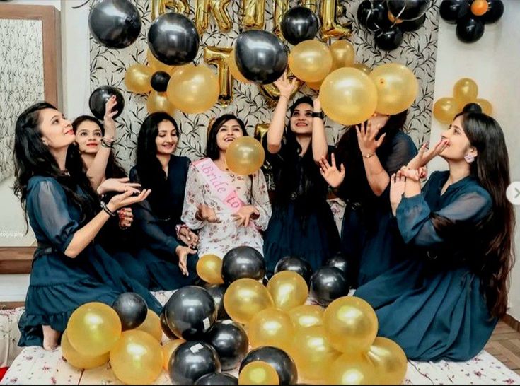 a group of women standing next to each other in front of black and gold balloons