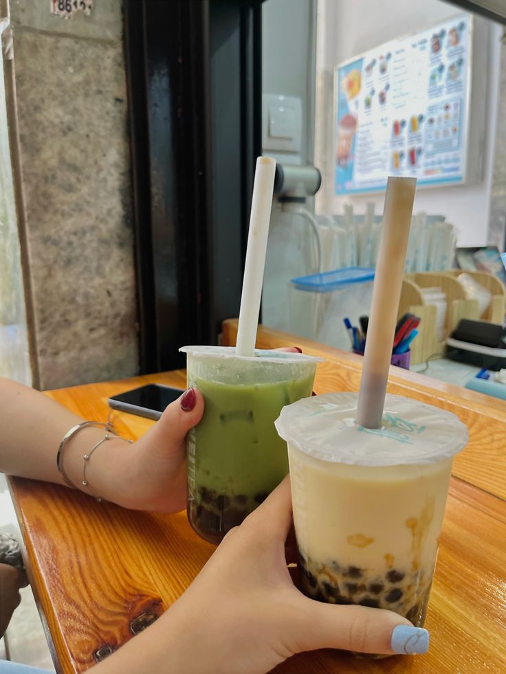 two people are holding up drinks at a table in front of a cell phone and another person's hand