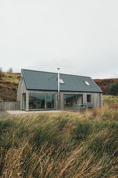 a house sitting on top of a lush green hillside next to tall grass and trees