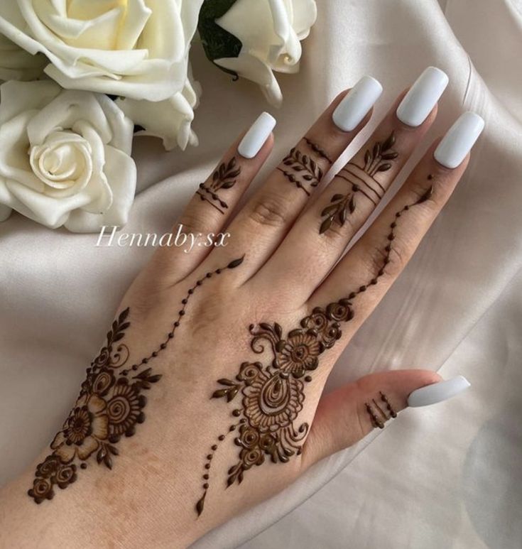 a woman's hand with henna tattoos on it and flowers in the background