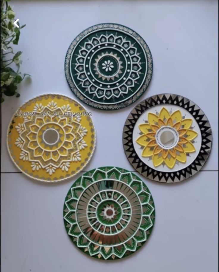 four plates with designs on them sitting next to a potted plant in the corner