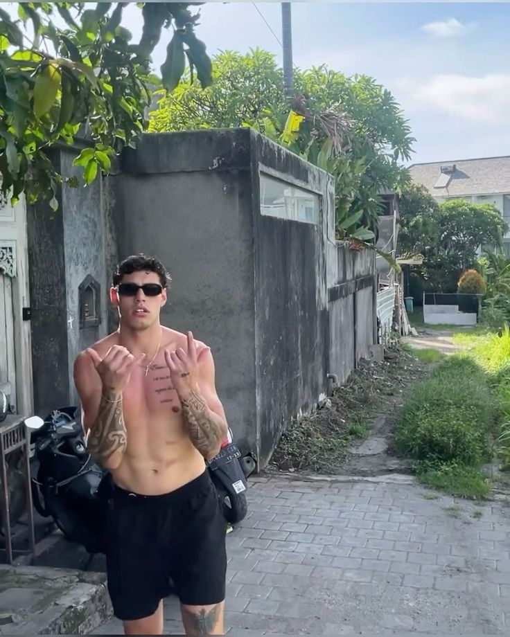 a man with no shirt on standing in front of a building holding his hands up to his chest