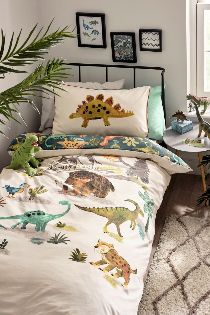 a bed room with a neatly made bed and dinosaur themed comforter sets on it